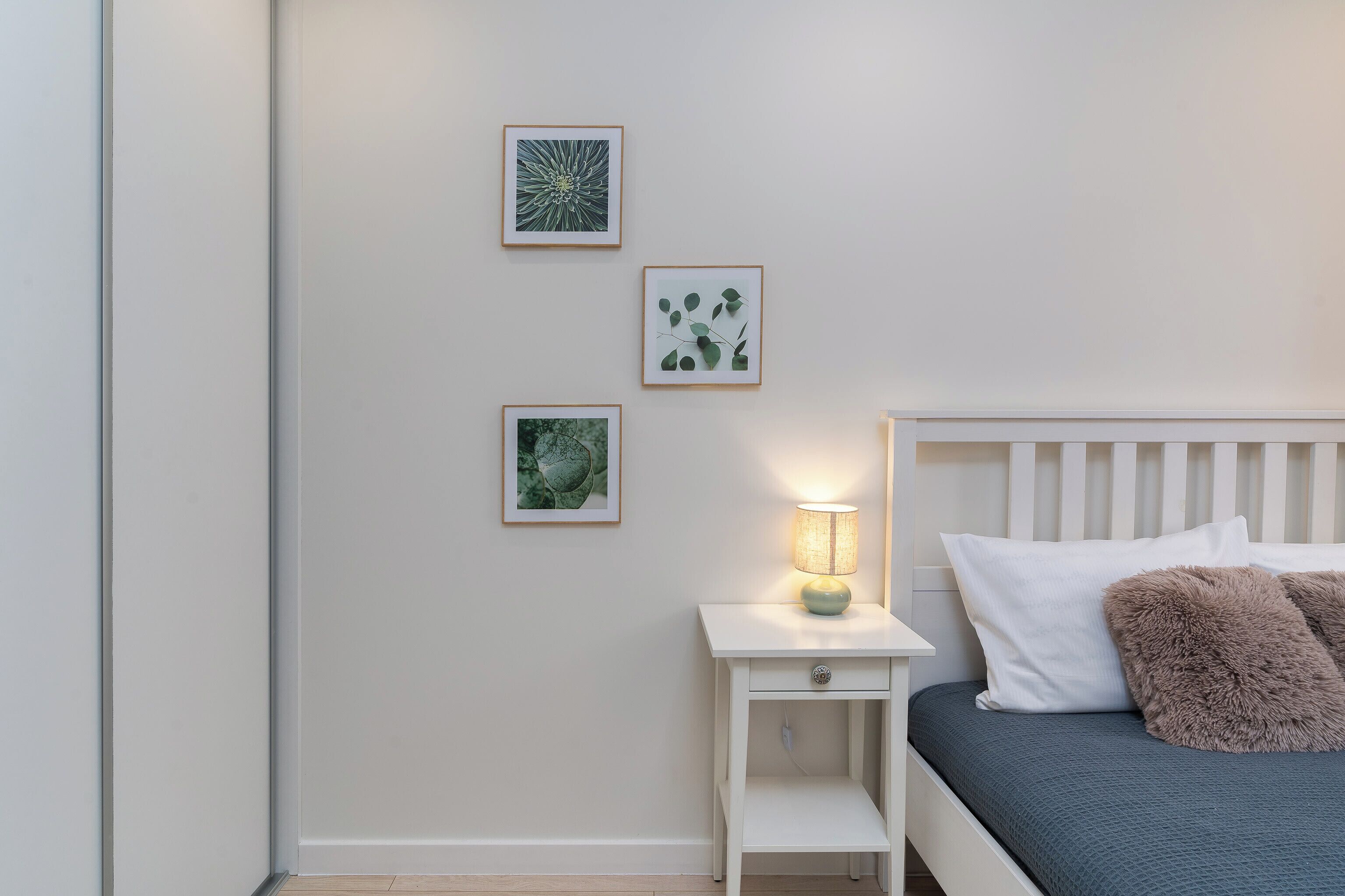 Une chambre à coucher avec un lit, une table de chevet avec une lampe et trois tableaux encadrés accrochés au mur.