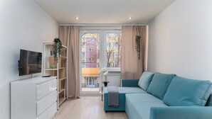 Un salon moderne avec un canapé de couleur turquoise, un meuble de rangement blanc et un téléviseur posé sur un meuble blanc.