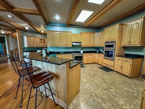 A spacious kitchen with wooden cabinets, a central island with bar stools, and built-in appliances. - The Iconic Red Roof Lakefront Estate of Deep Creek Lake - 8BR, Sleeps 20 (McHenry)