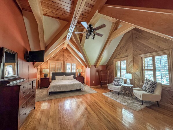 A spacious attic bedroom with a large bed, a ceiling fan, and a TV mounted on the wall. - The Iconic Red Roof Lakefront Estate of Deep Creek Lake - 8BR, Sleeps 20 (McHenry)