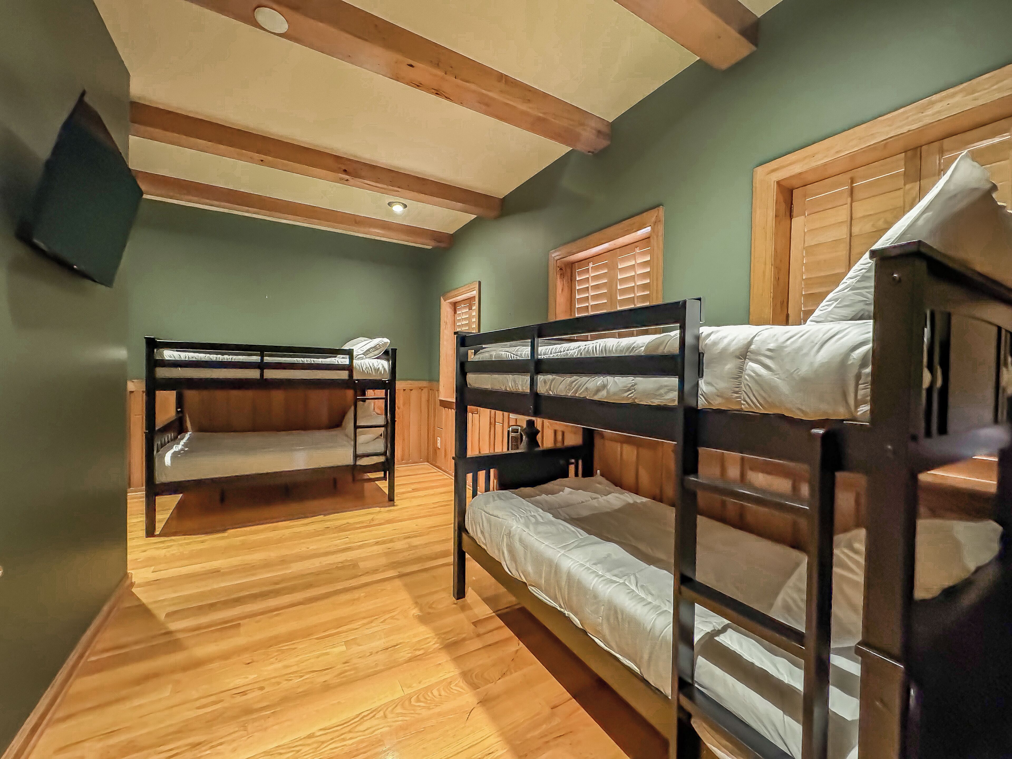 Una habitación con dos literas, suelo de madera y techo inclinado con vigas a la vista.