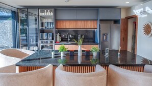 A modern kitchen with a built-in oven, microwave, and stainless steel refrigerator. There is a wooden cabinet above the sink and a glass display case with kitchenware. - Stunning 4BR Luxury Retreat w Private Rooftop Pool (Playa Del Carmen)