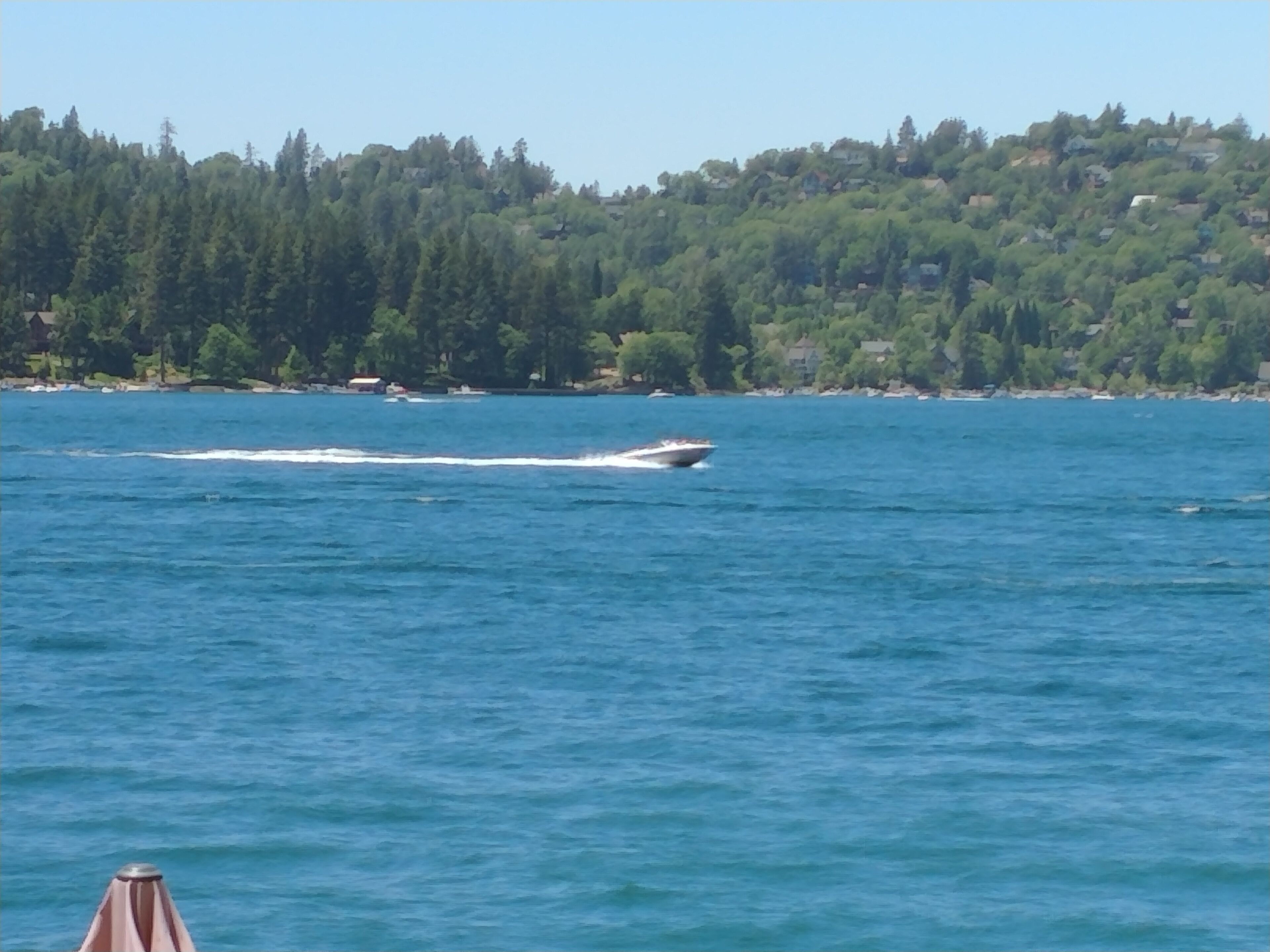 Un bateau navigue sur une étendue d’eau calme, avec une colline boisée en arrière-plan.