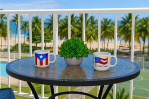 Ett runt bord med två muggar prydda med Puerto Ricos flagga, en krukväxt och en utsikt över palmer och en strand.