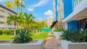 Un patio de hotel con un camino empedrado, palmeras y vistas de otros edificios al fondo.