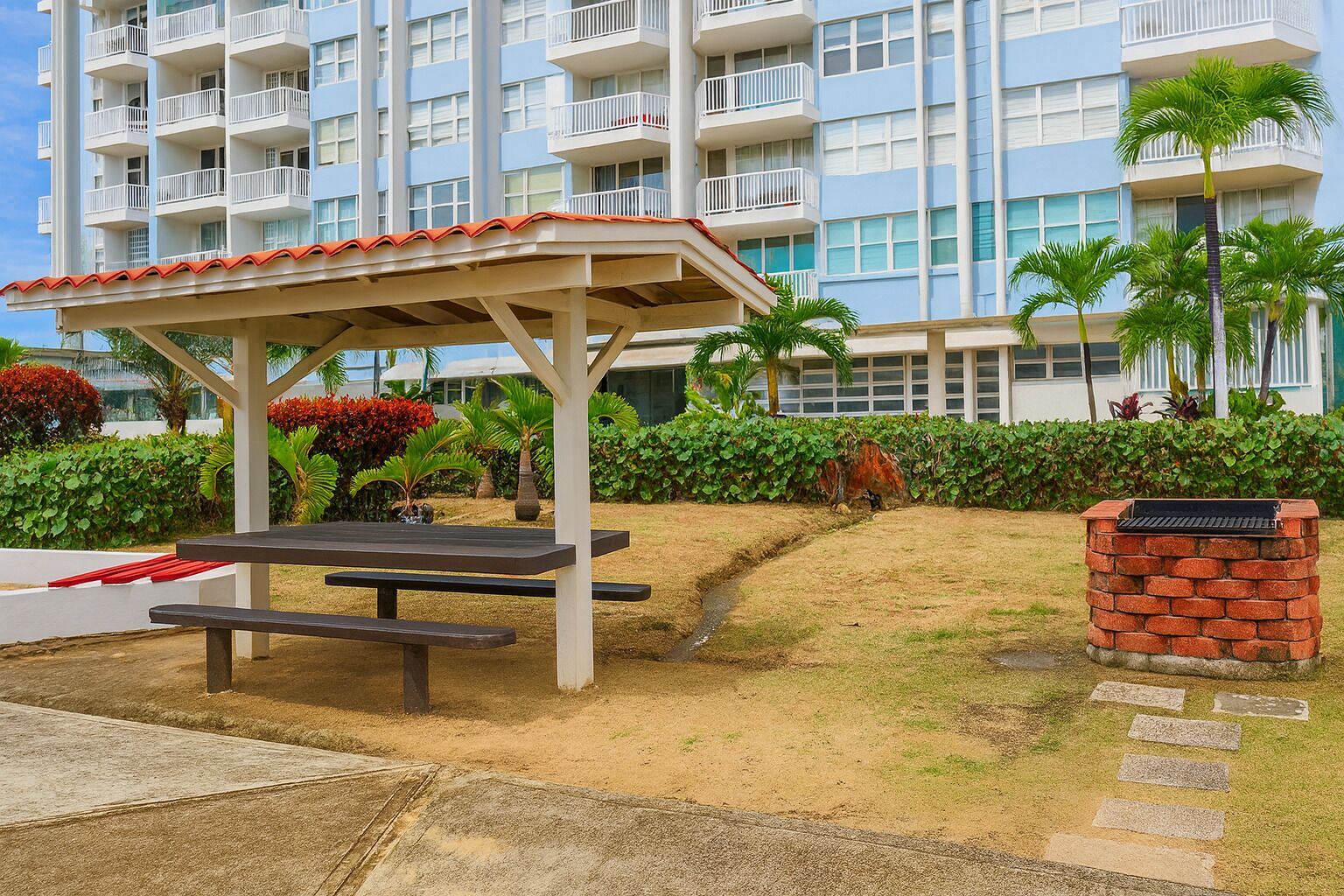 A covered picnic area with benches, a brick planter, and a pathway leading to a building with balconies.