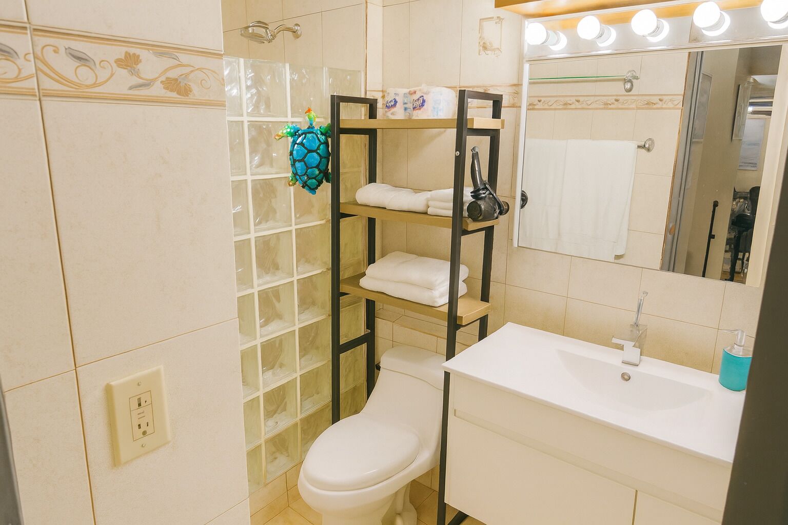 A bathroom with a toilet, a sink, a mirror, and a shelf with towels.