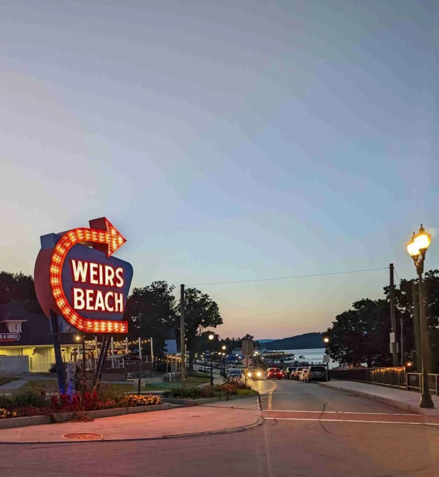 Un panneau indiquant « Weirs Beach », avec une flèche distinctive et des lettres illuminées.