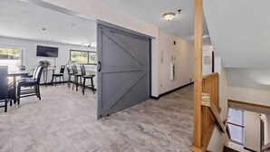 Una habitación amplia con un gran ventanal corredero, una zona de comedor con sillas y una mesa, y una escalera con barandillas de madera.