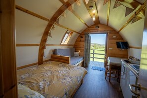 A cozy, wooden interior with a bed, a desk, and a view through a door.
