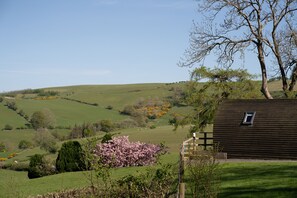 A rural landscape with rolling green hills, a wooden house with a small window, and a tree with bare branches.