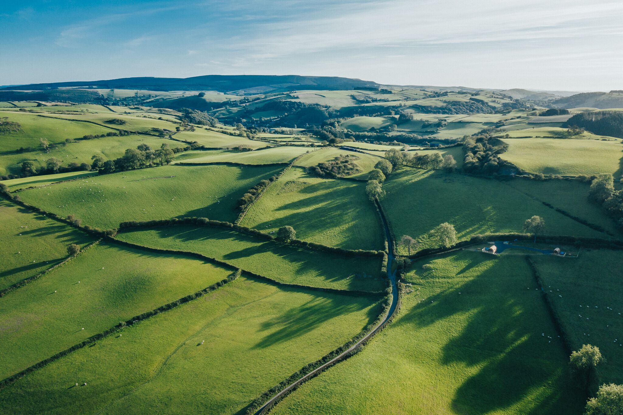 A rural landscape with rolling green fields, stone walls, and a narrow road.