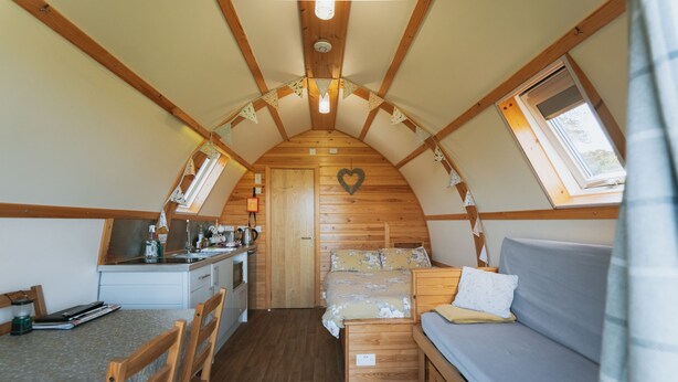 A compact, well-lit room with a kitchenette, a bed with a floral bedspread, and a sofa.