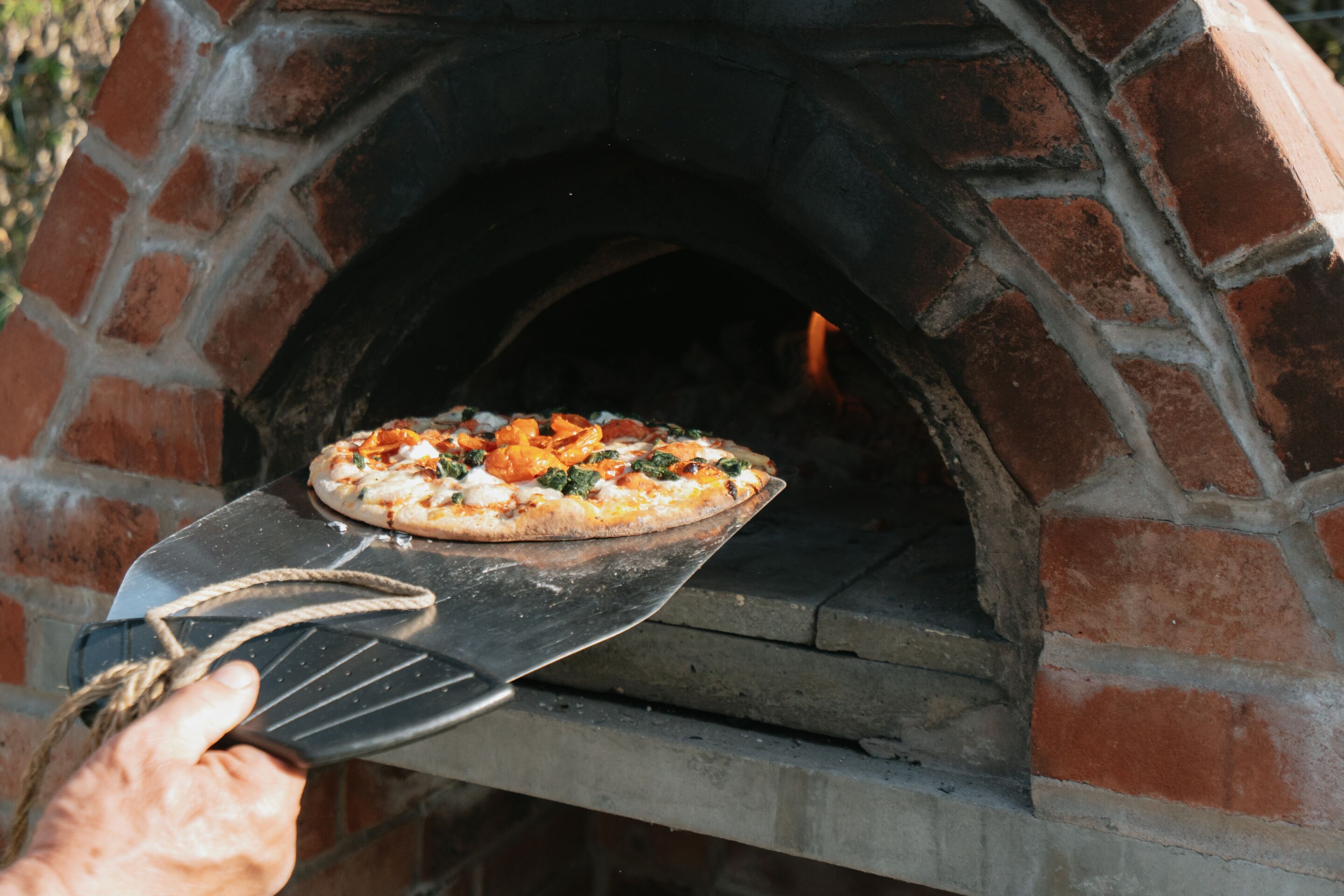 On sort une pizza d’un four en briques.