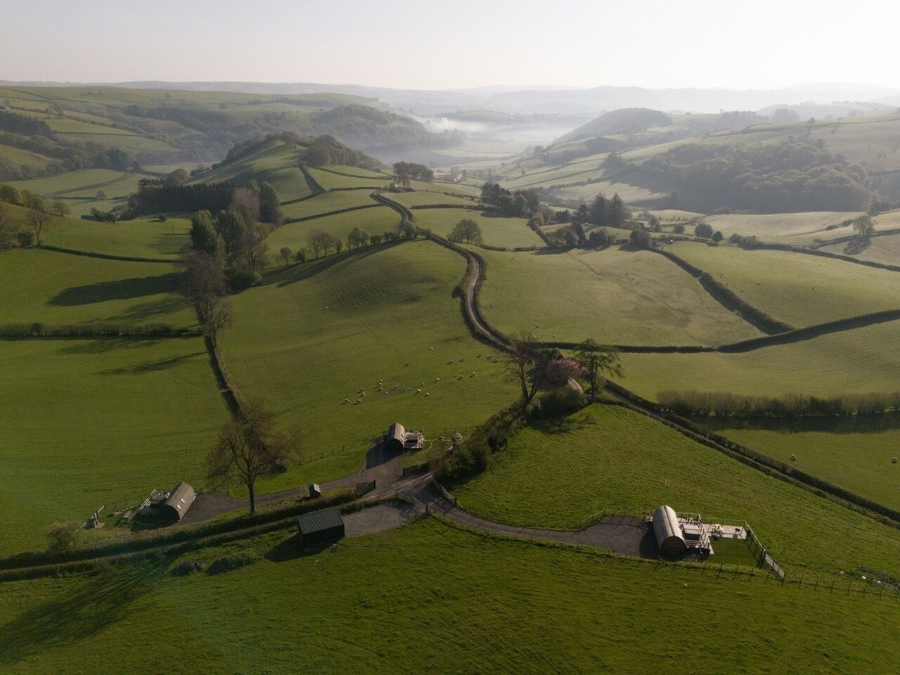 A rural landscape with rolling hills, a winding road, and a few buildings.