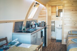 A compact kitchen with a window, a sink, and a small dining area. - Rural Welsh Cabin with Spectacular Views (Knighton)