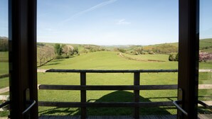 A view through a wooden-framed window of a green field with a clear sky. - Rural Welsh Cabin with Spectacular Views (Knighton)