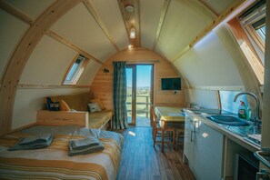 Un alojamiento acogedor de una sola habitación con cama en altillo, una kitchenette pequeña y vistas a un espacio exterior a través de una puerta.