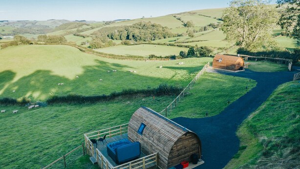 A wooden cabin with a loft bed and a small deck, surrounded by a fenced pasture with grazing sheep. - Rural Welsh Cabin with Spectacular Views (Knighton)