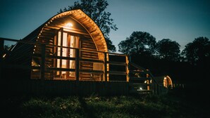 A wooden cabin with a curved roof and large windows, surrounded by trees. - Rural Welsh Cabin with Spectacular Views (Knighton)