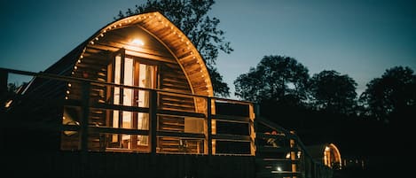A wooden cabin with a curved roof and large windows, surrounded by trees.