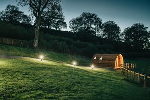 A wooden cabin with a sloped roof, surrounded by a grassy field and trees. - Rural Welsh Cabin with Spectacular Views (Knighton)