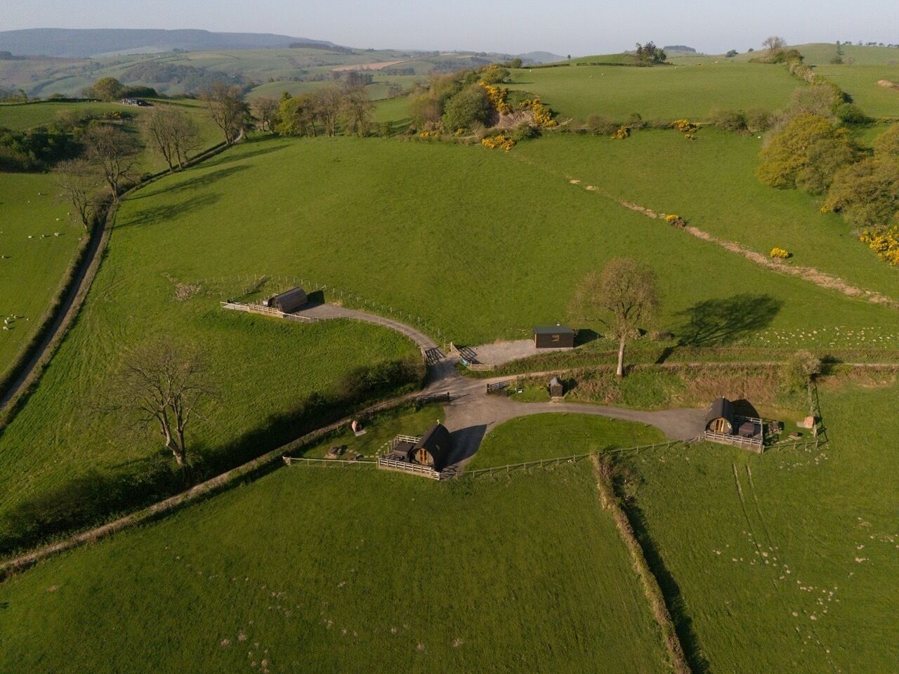 An aerial view of a rural property with a central road, fenced areas, and scattered buildings.