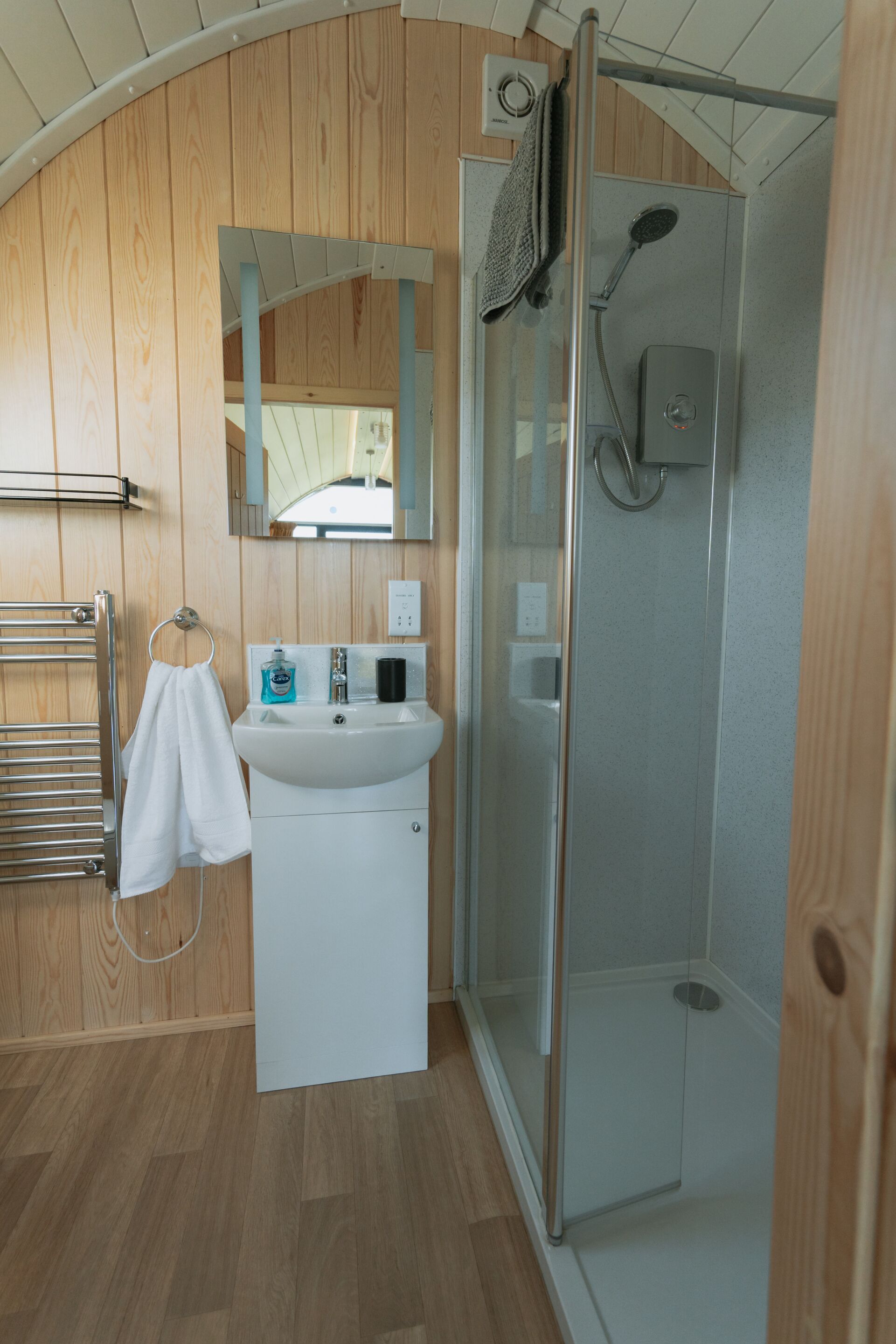 A bathroom with a wooden panel wall, a white sink, a towel rack, a glass shower enclosure, and a mirror.