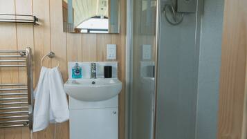 A bathroom with a wooden panel wall, a white sink, a towel rack, a glass shower enclosure, and a mirror.