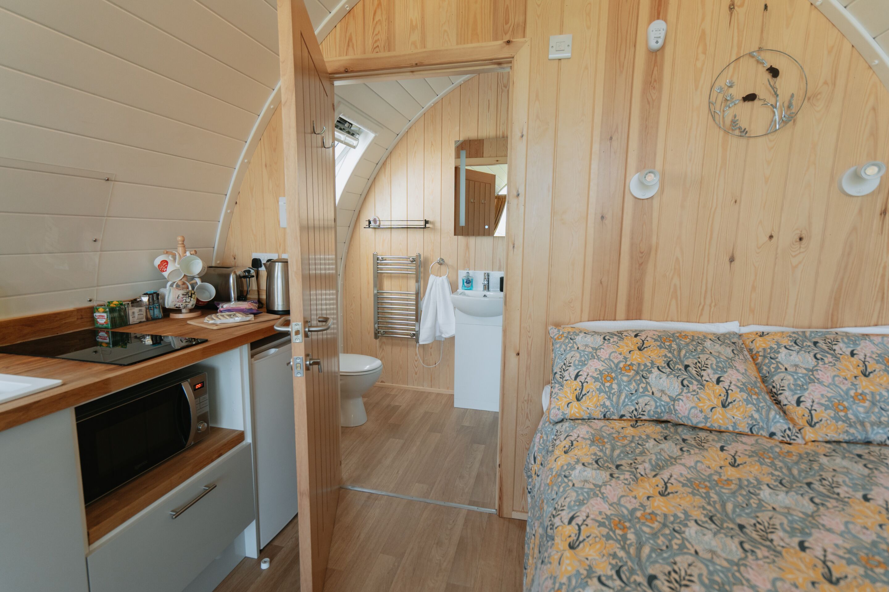 Un intérieur compact en bois, comprenant un coin cuisine, une salle de bain et un lit avec une literie à motifs floraux.