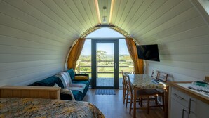 Ein gemütliches Zimmer mit einem Bett, einem Schreibtisch und einem Fernseher. Es hat ein großes Fenster und eine Tür, die nach draußen führt.