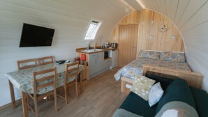 Ein kompakter, bogenförmiger Raum mit Küchenzeile, einer Essecke mit Tisch und Stühlen sowie einem Bett mit gemustertem Überwurf.