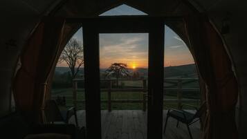 A room with a large window, a wooden deck outside, and a view of the sunset.