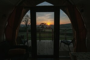 Una habitación con un gran ventanal, una terraza de madera en el exterior y vistas al atardecer.