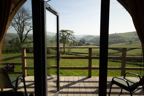 Une terrasse en bois ouverte, offrant une vue sur des collines verdoyantes et des arbres.