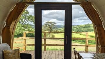 Une pièce confortable avec une terrasse en bois, un lit et une table, offrant une vue imprenable sur un paysage verdoyant et des collines.
