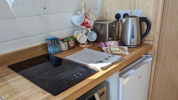 Eine kompakte Küche mit integriertem Induktionskochfeld, einer Mikrowelle, einer Kaffeemaschine und einem Toaster.