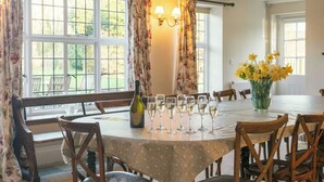 Un coin repas avec une table ronde, des chaises, des rideaux à motifs floraux et un vase rempli de fleurs jaunes.