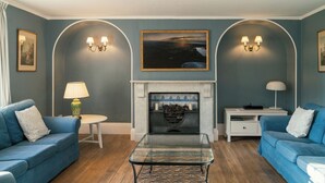 Un salon avec deux canapés bleus, une table basse en verre, une cheminée dont le foyer est orné de carreaux bleus, et des appliques murales.