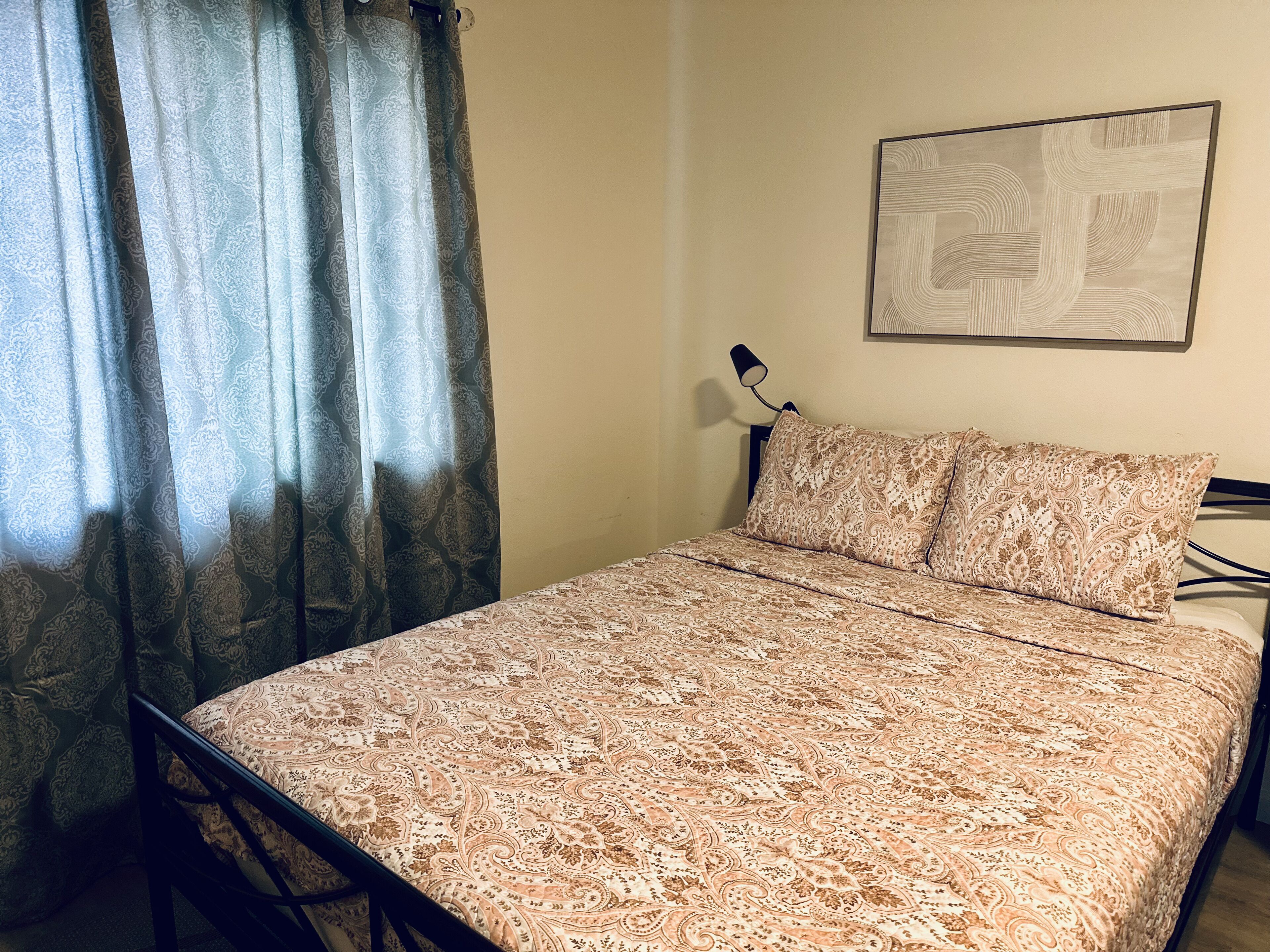 Un letto con copripiumino decorato, una lampada da comodino e un'opera d'arte appesa al muro.