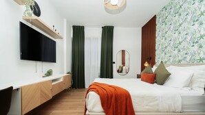Een moderne slaapkamer met een bed, een aan de muur bevestigde televisie, een nachtkastje en een spiegel.