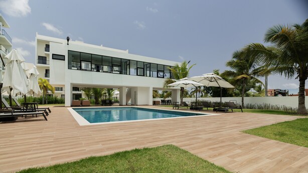 Een modern gebouw met een zwembad, terras en palmbomen.