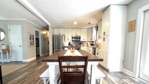 A modern kitchen with white cabinets, a central island, and a dining area with white chairs. - Near ILM Family Gathering Home, Sleeps up to 8, host up to 12. Your Holiday spot (Wilmington)