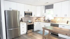 A modern kitchen with white cabinets, stainless steel appliances, a wooden table, and a tiled backsplash. - Near ILM Family Gathering Home, Sleeps up to 8, host up to 12. Your Holiday spot (Wilmington)