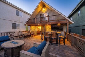 Une maison à deux étages dotée d’une terrasse, de meubles d’extérieur et d’un téléviseur fixé au mur.