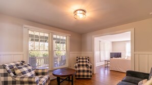 Una sala de estar con un sillón a cuadros, un sofá oscuro y una mesa redonda de madera.