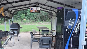 A covered outdoor area with a grill, seating, and a beverage dispenser. - Regency Inn (Jewett)