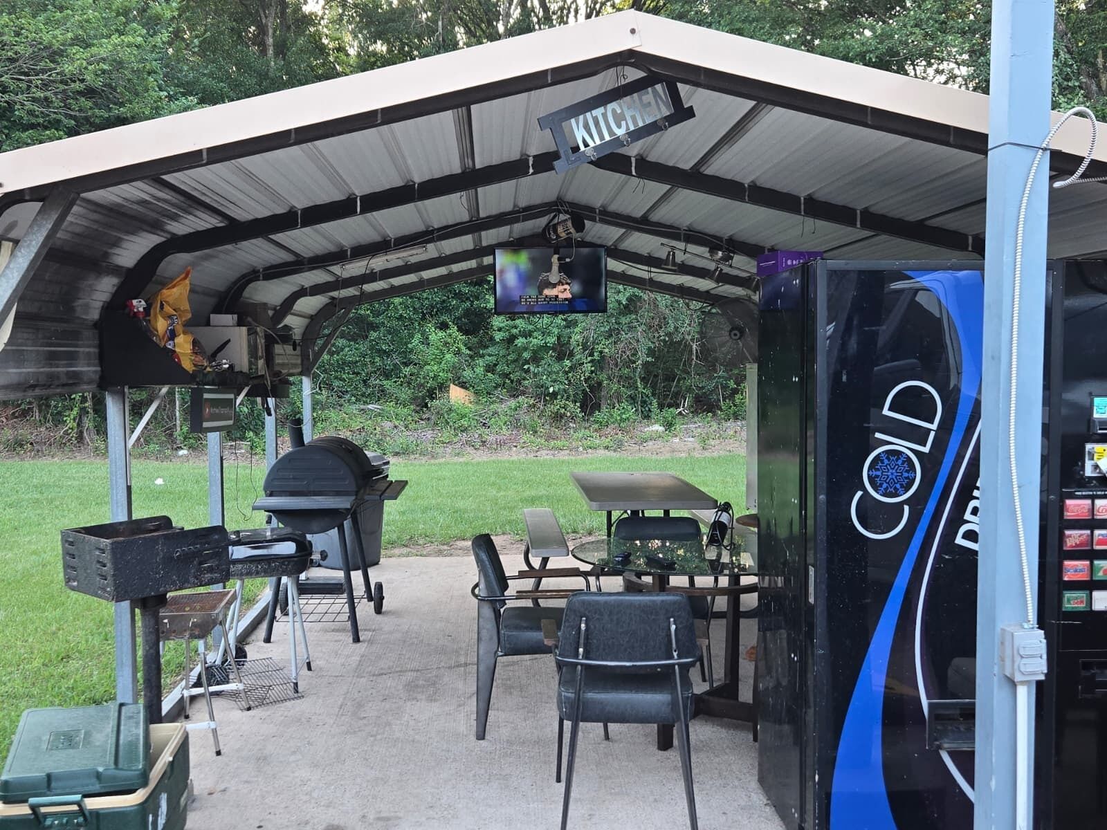 A covered outdoor area with a grill, seating, and a TV screen.