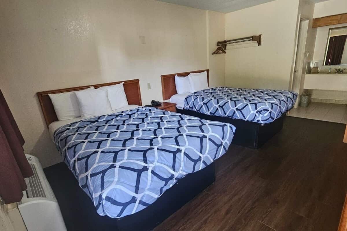 A hotel room with two beds, a wooden floor, a small table, and a mirror.