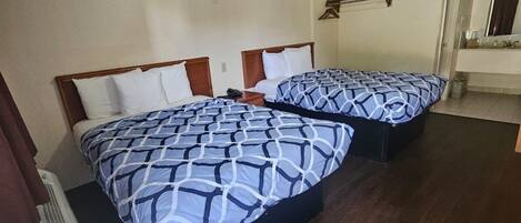 A hotel room with two beds, a wooden floor, a small table, and a mirror.